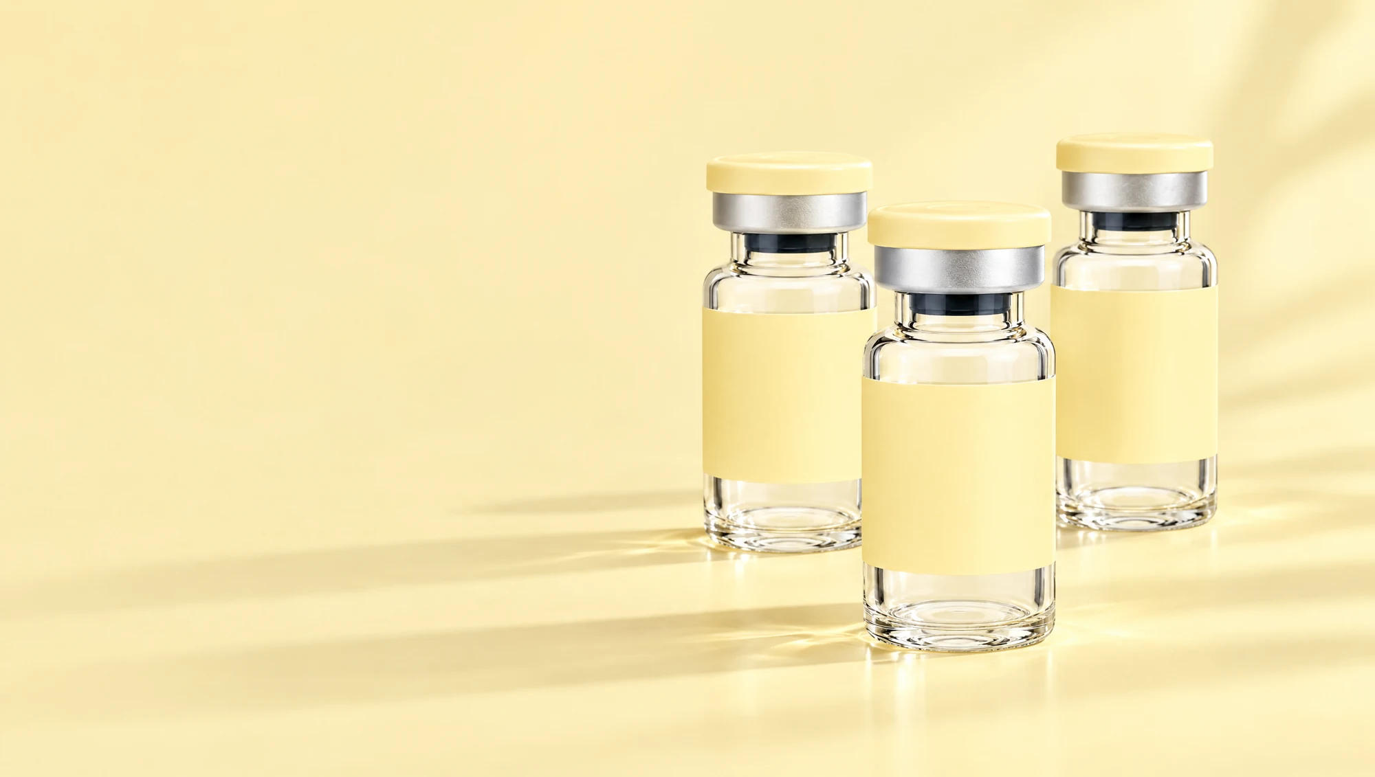 Three clear vials with pale yellow labels arranged in sunlight on a pale yellow surface
